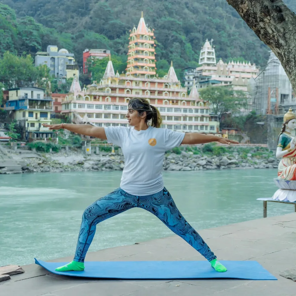 Student in warrior two pose with the temples of Rishikesh behind