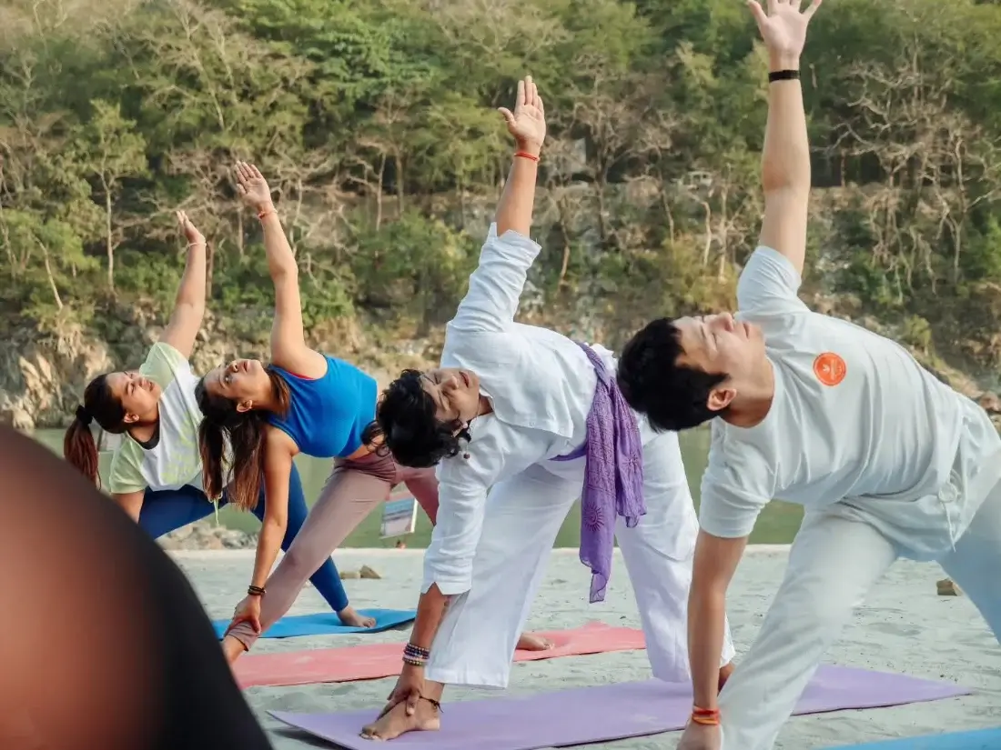 Students holding reverse warrior pose during a riverside class in Rishikesh