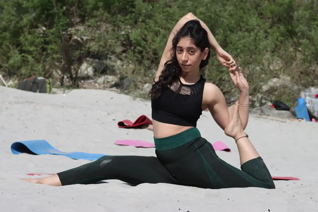 Student in one legged king pigeon pose on the sand at Rishikesh Yog Kendra