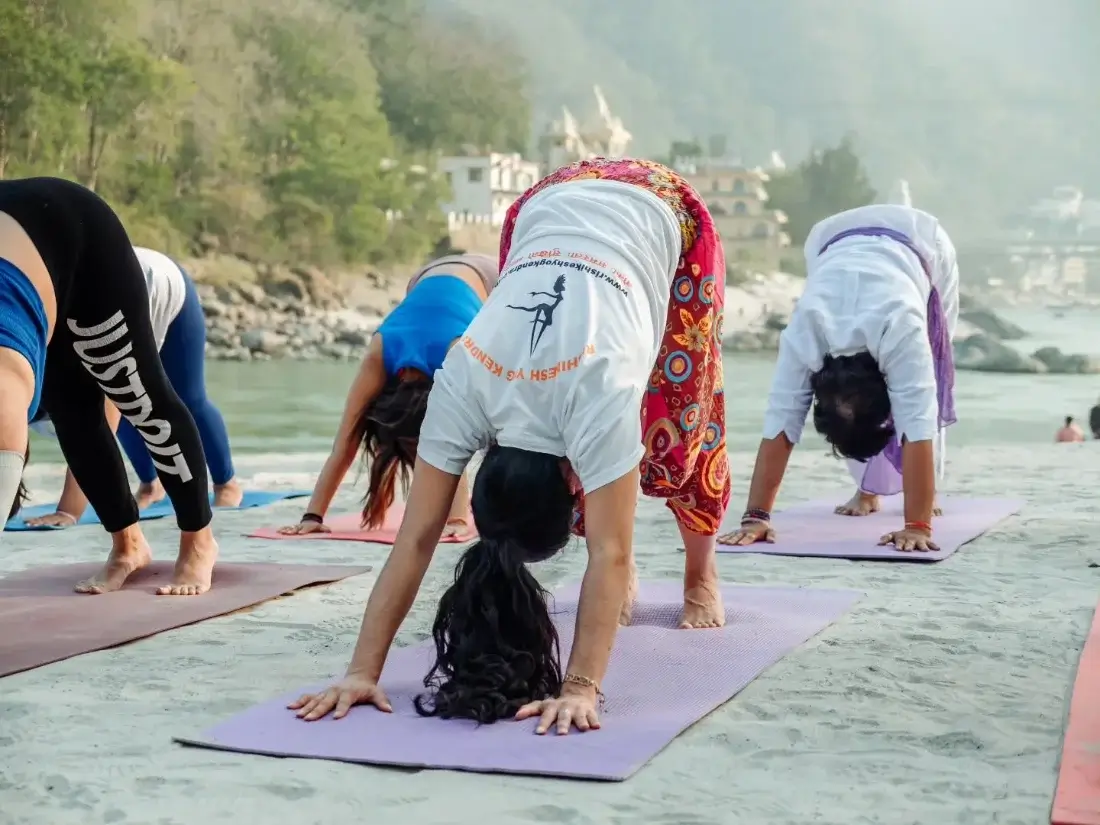 Students in downward facing dog beside the Ganga with Rishikesh behind