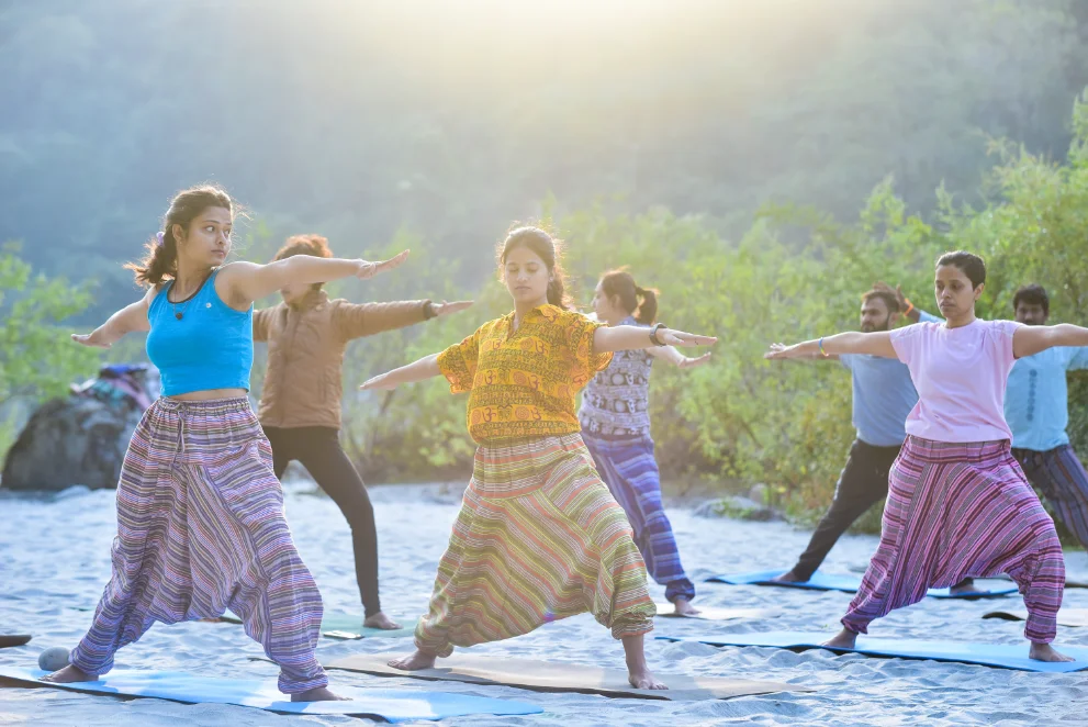 Students holding warrior two pose at sunrise on the river bank