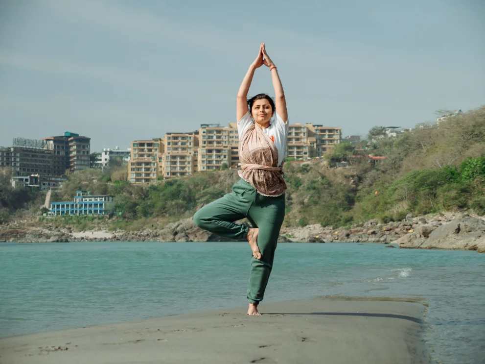 Student in tree pose on the sandbank with Rishikesh behind