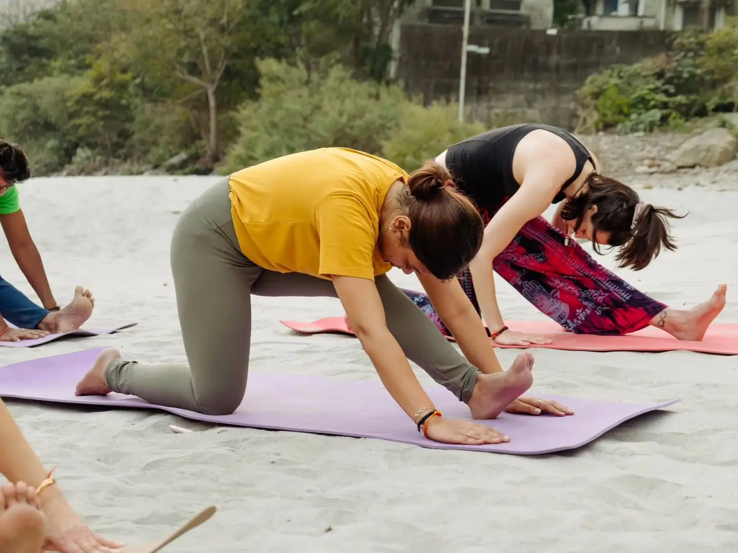 Two students practising a kneeling forward stretch with close guidance on the sand