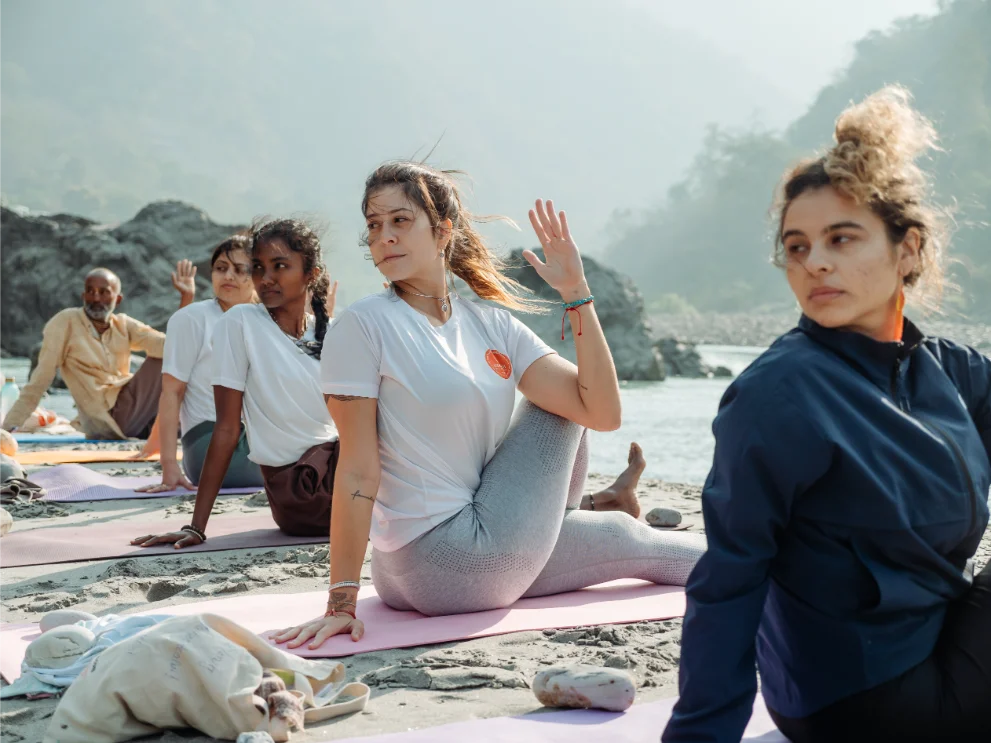 Small group holding a seated spinal twist with their teacher beside the Ganga