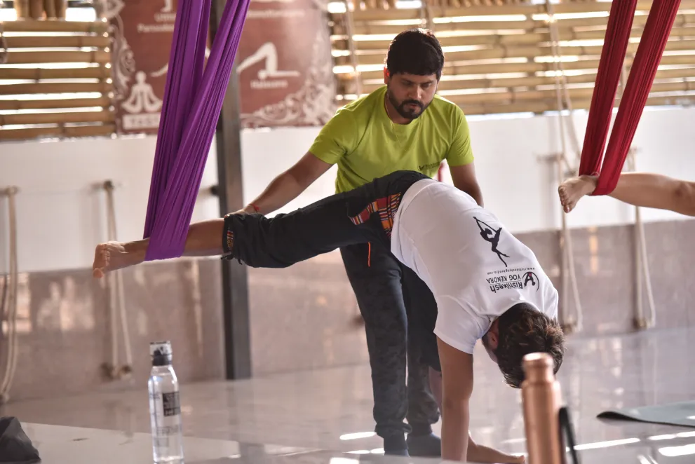 Teacher adjusting a student hands-on through a supported backbend in the hammock