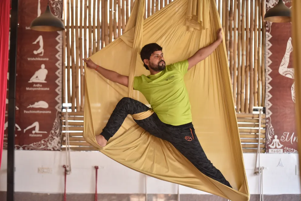 Teacher seated in the hammock in the school&rsquo;s aerial hall, asana charts along the wall