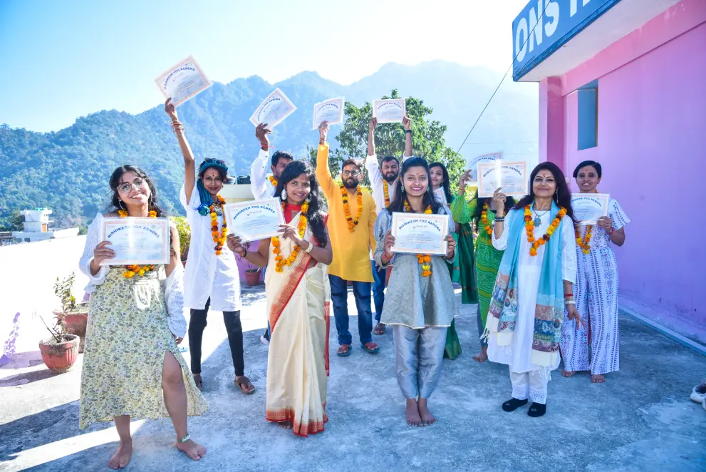Graduates holding their Rishikesh Yog Kendra certificates in the morning sun with the Rishikesh hills behind them