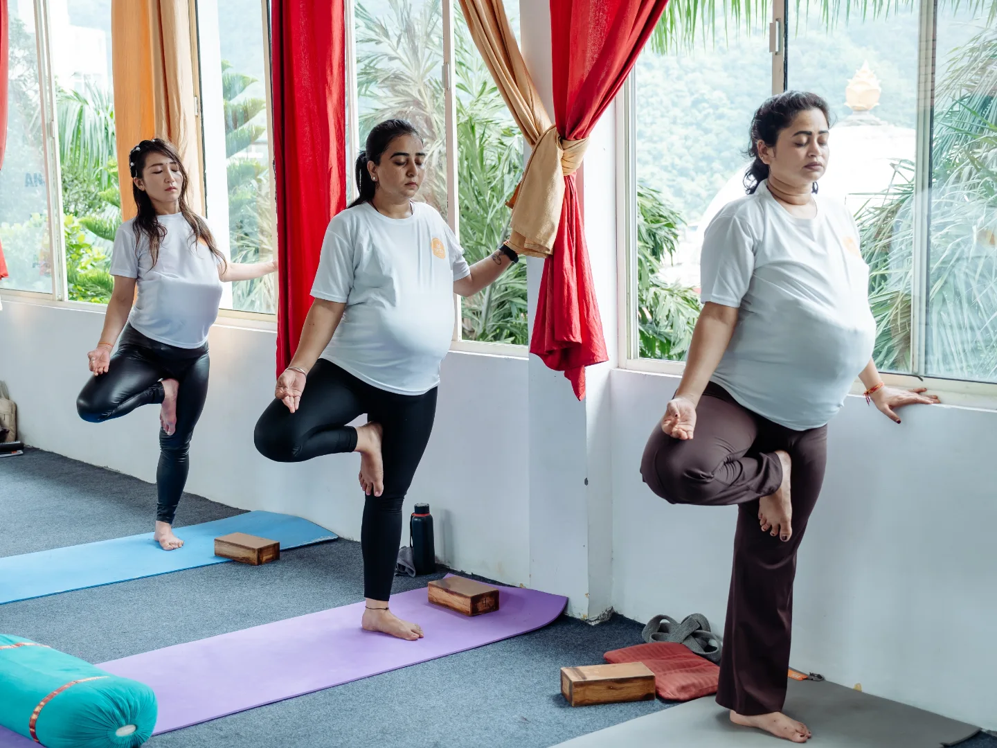Pregnant students holding a supported tree pose in the prenatal yoga class in Rishikesh