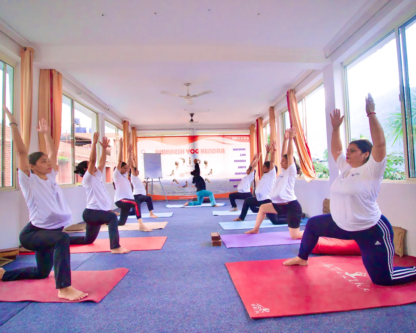 Full prenatal yoga class practising low lunge in the Rishikesh Yog Kendra hall