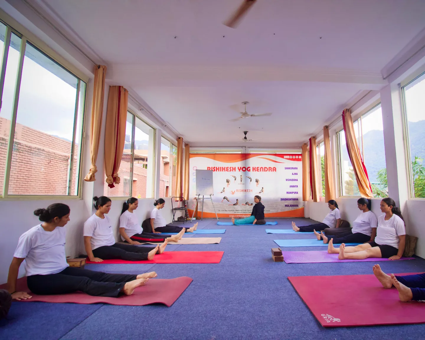 Full class seated in the Rishikesh Yog Kendra practice hall with the teacher leading from the front