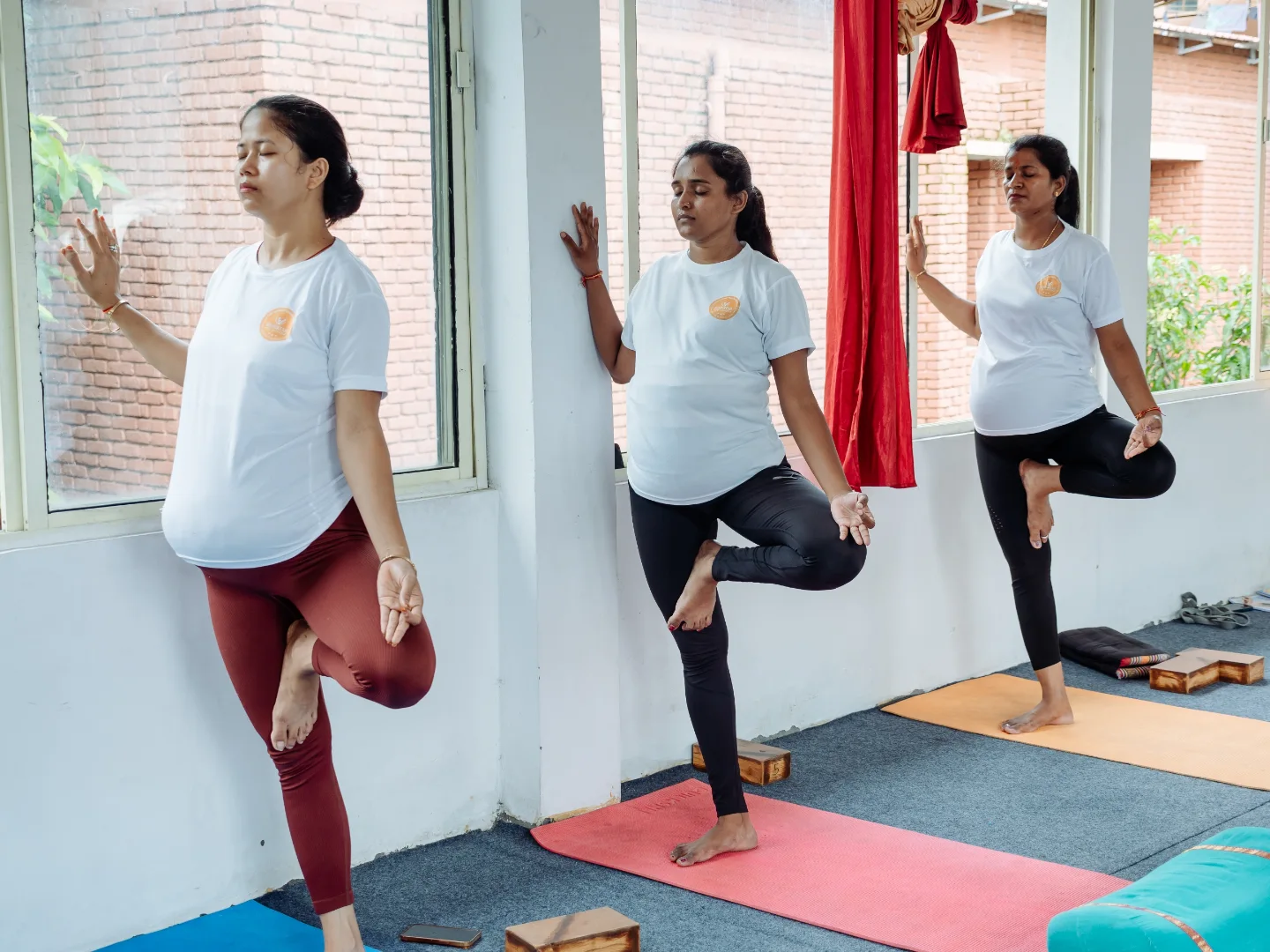 Three expecting mothers balancing in a wall-supported tree pose