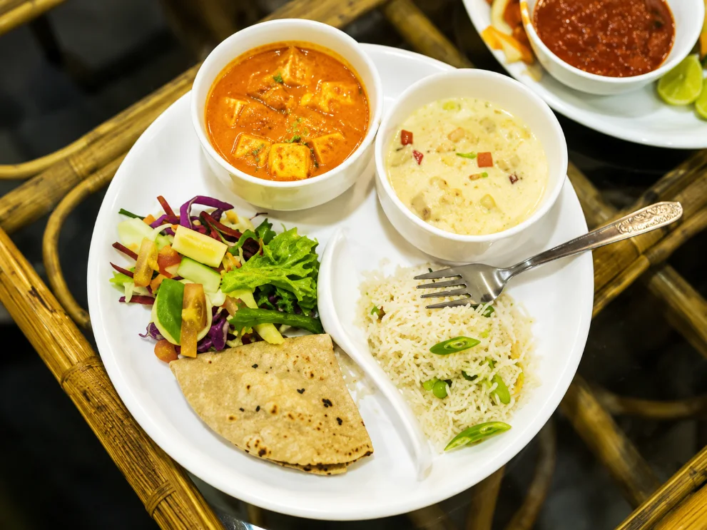 Plate of paneer curry, herbed rice, fresh salad and chapati