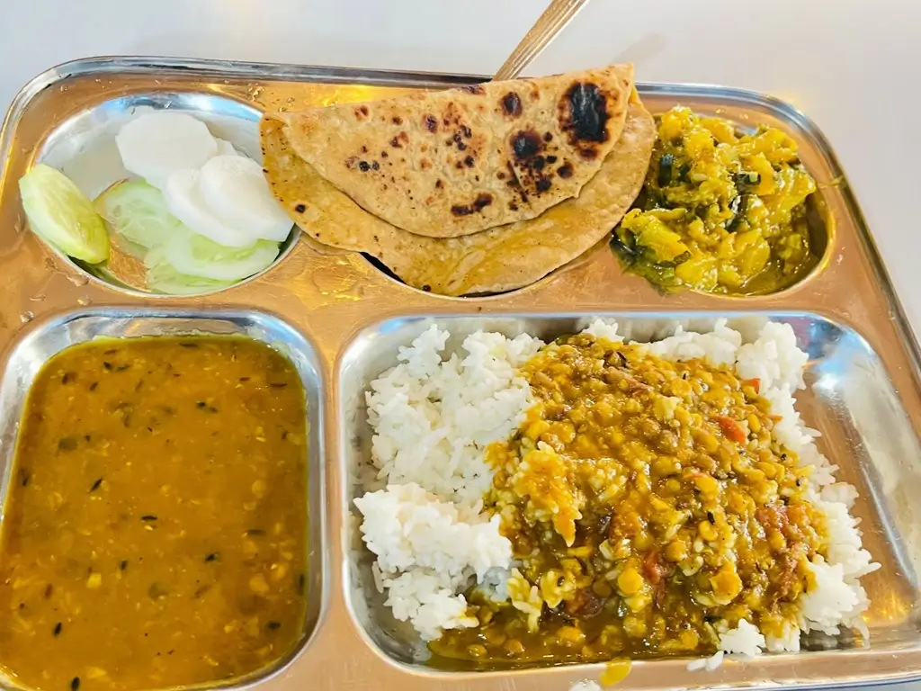 Steel thali with roti, dal, rice, seasonal sabzi and cucumber salad
