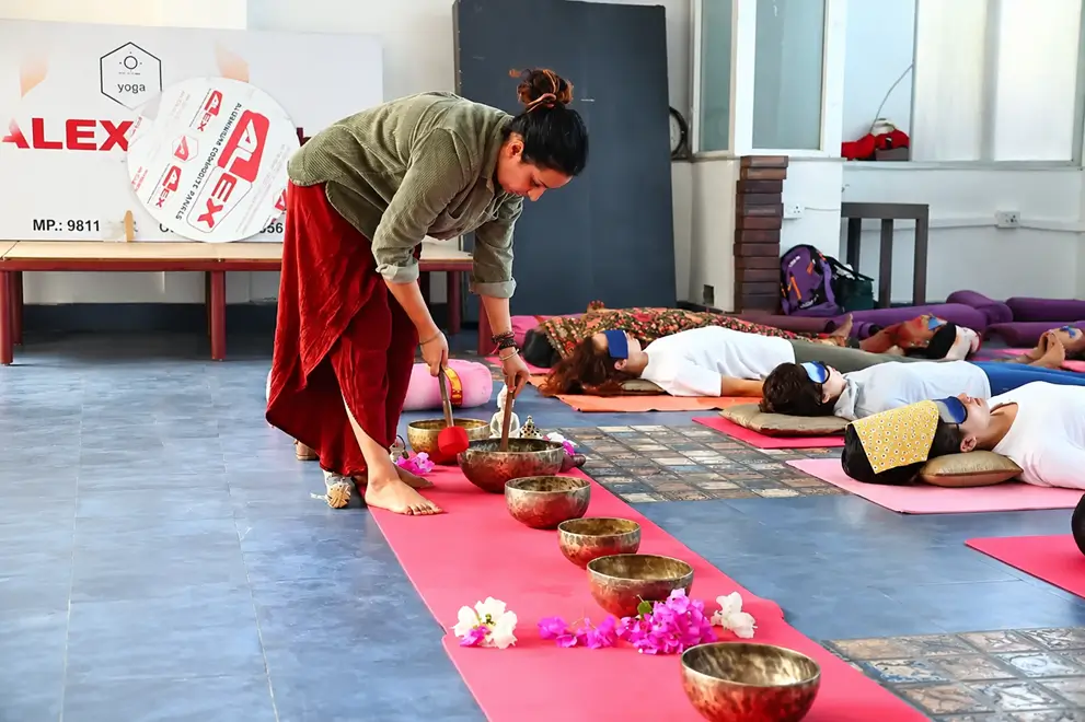 Teacher playing singing bowls laid along a mat while students rest through a sound healing session in Rishikesh