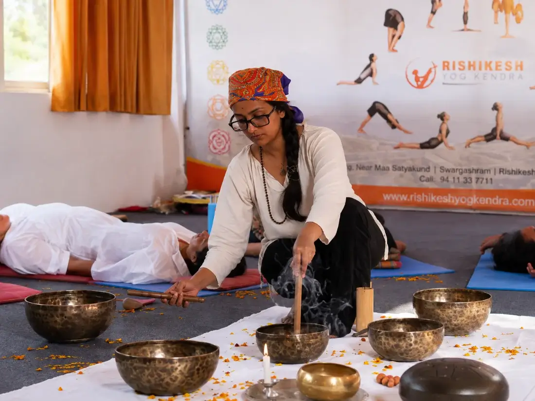 Teacher seated among singing bowls with incense and marigold petals laid out for the session