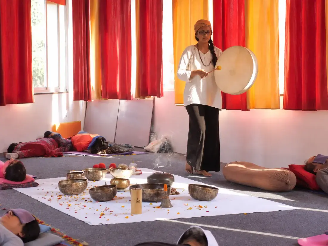 Teacher playing a frame drum over a laid-out set of singing bowls