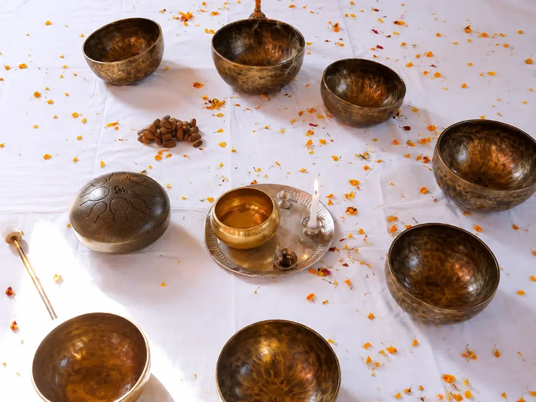 Singing bowls, tongue drum, tingsha and candle laid out ready for a session