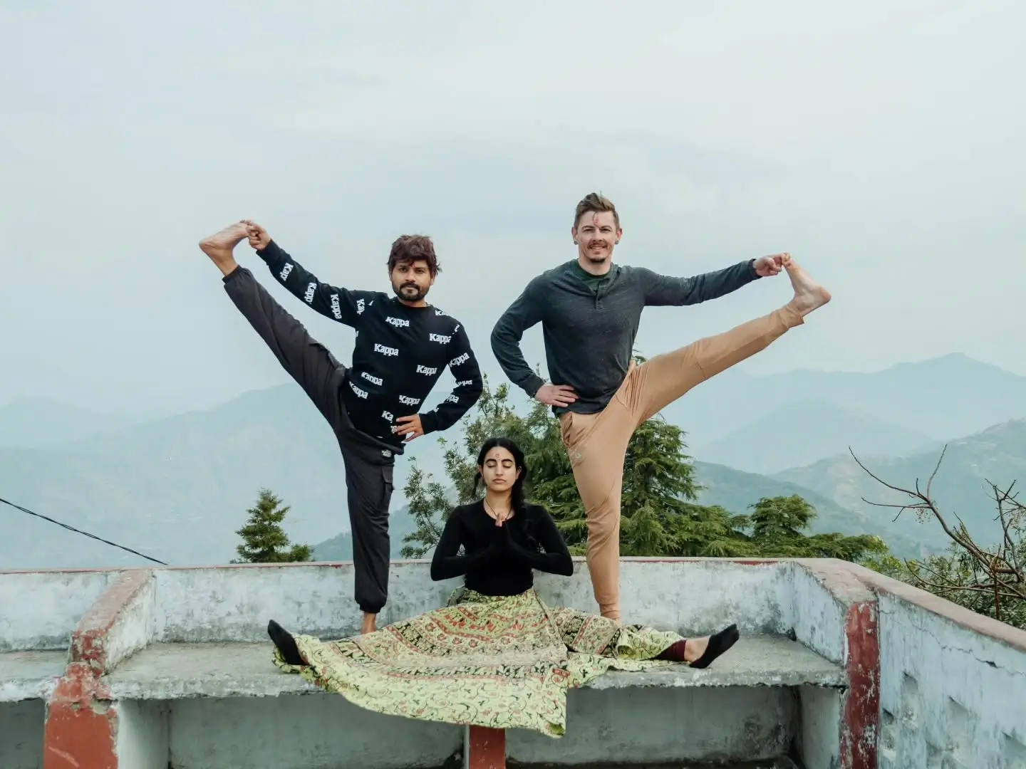 Students practising on a rooftop above Rishikesh with the Himalayan foothills behind them
