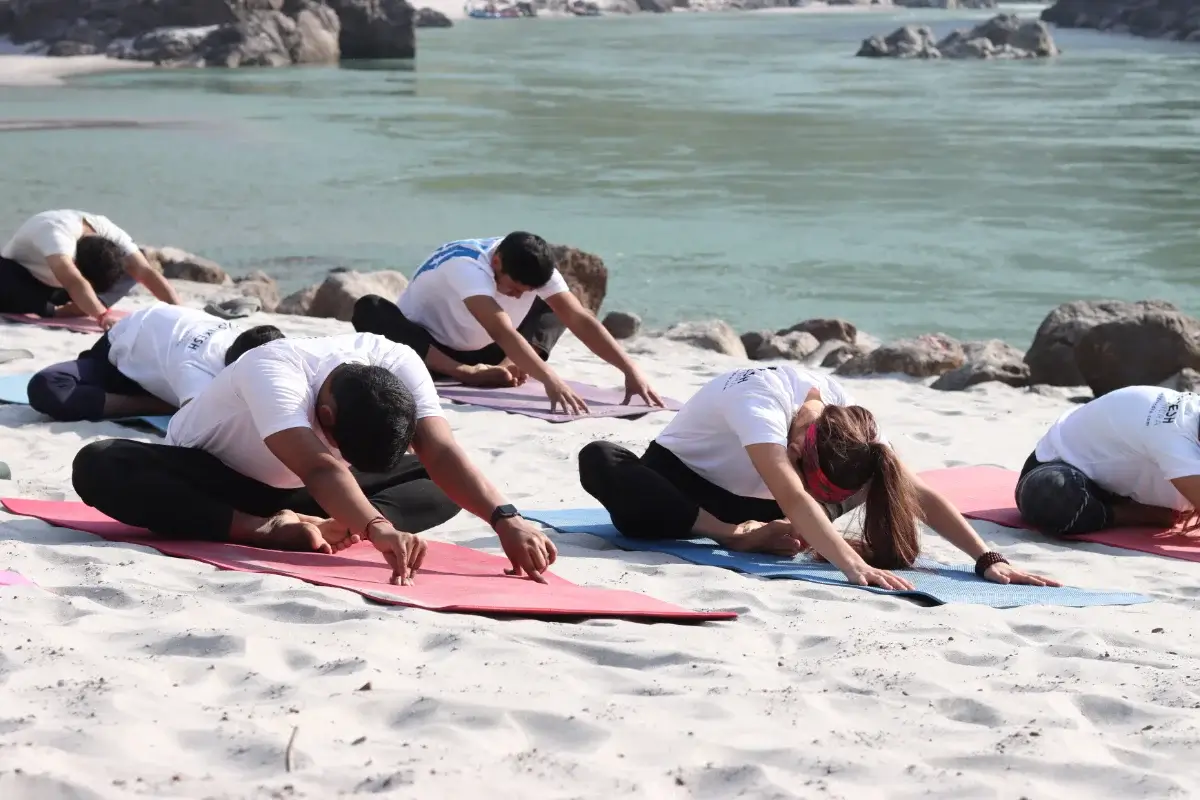Students settling into a long-held forward fold on the sand beside the Ganga